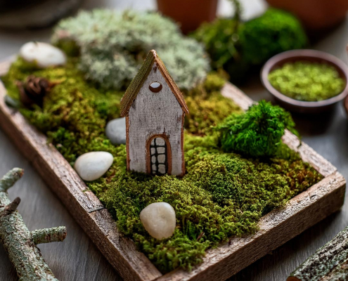 Wooden tray fairy garden with moss, simple rustic house and pebbles.