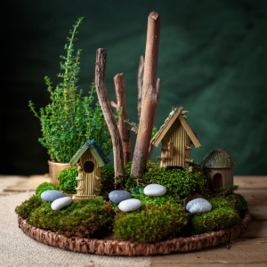 Lovely fairy garden denoting woodland scene with corrugated cardboard and stick houses, twig trees, sticks, pebbles, and moss.