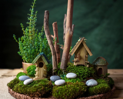 Lovely fairy garden denoting woodland scene with corrugated cardboard and stick houses, twig trees, sticks, pebbles, and moss.