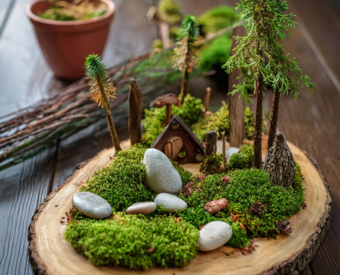 Fairy garden on a log slice with simple rustic house, moss, pebbles, sticks and pretend trees.