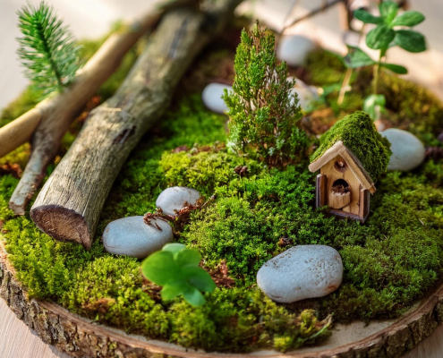 Fairy garden on a log slice with moss, pebbles, sticks and pretend trees.