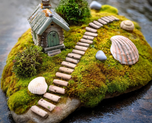 Fairy garden on a rock with pebble path, seashells and little house.