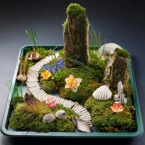 Fairy garden on a metal tray with seashells, feature rocks, flower heads and stick path.